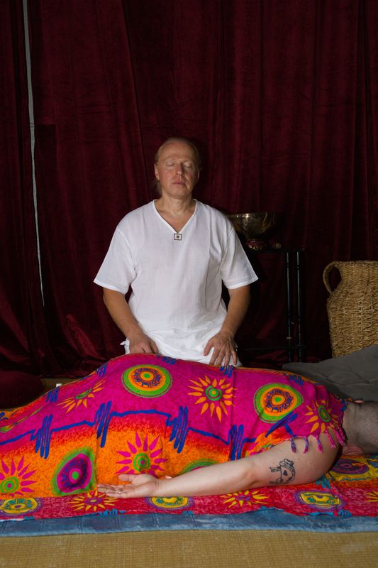 Sergio sitting with his eyes closed and his hands resting on a client who lies under a bright orange and pink sarong